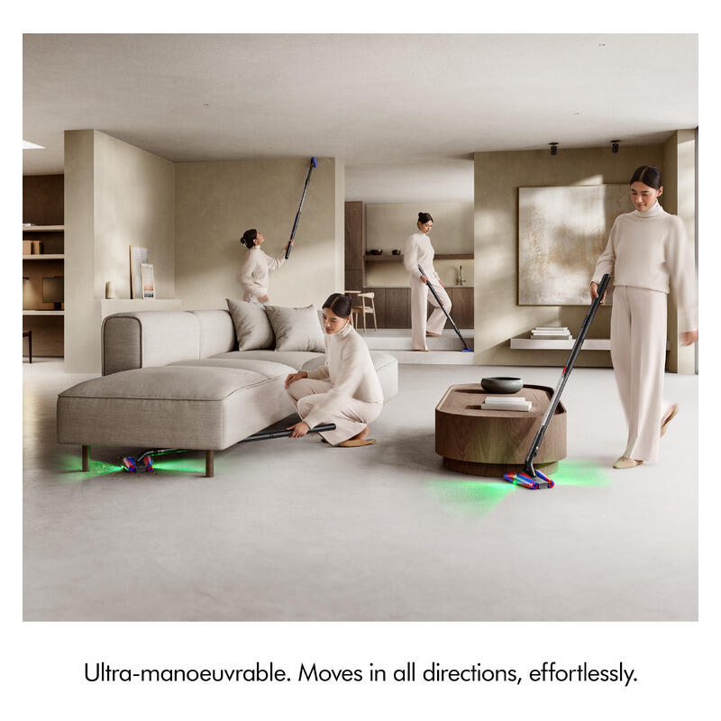Three women in matching cream loungewear clean a modern open-plan apartment with a long-handled floor mop and a small floor sweeper, with green floor light accents. The scene includes a gray sectional sofa, a round wooden coffee table, and a large abstract painting on the wall.