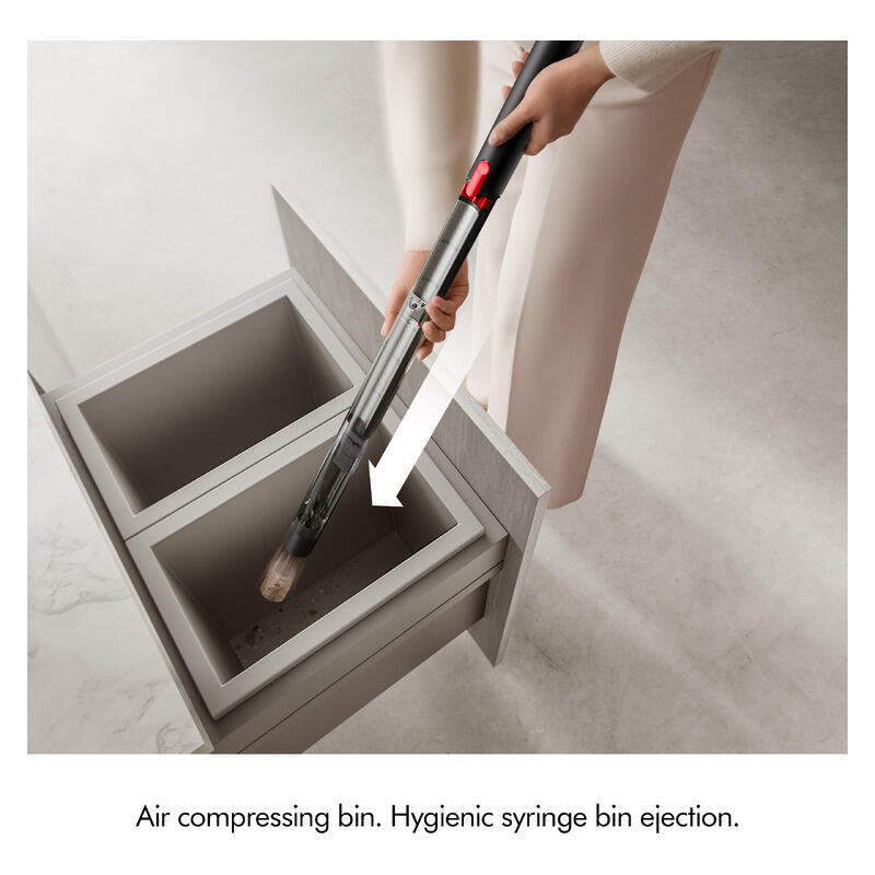 A person uses a handheld vacuum cleaner to empty a dual-basin hygienic syringe bin drawer. The text at the bottom reads: 'Air compressing bin.