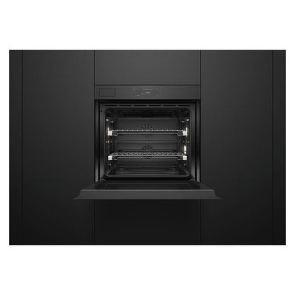 A built-in wall oven shown from the front with its door open, revealing two interior racks and lit oven lights, set against a dark charcoal kitchen cabinet background.