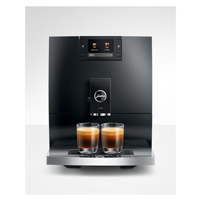 A black Jura commercial espresso machine with two glass cups of espresso on its drip tray, set against a light gray studio background.