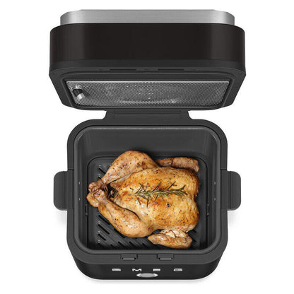 A black and stainless steel smeg air fryer with its lid open, shown cooking a whole roasted chicken inside the basket on a white background.