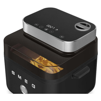 Black and silver SMEG air fryer with a transparent window showing french fries inside, on a clean white background.