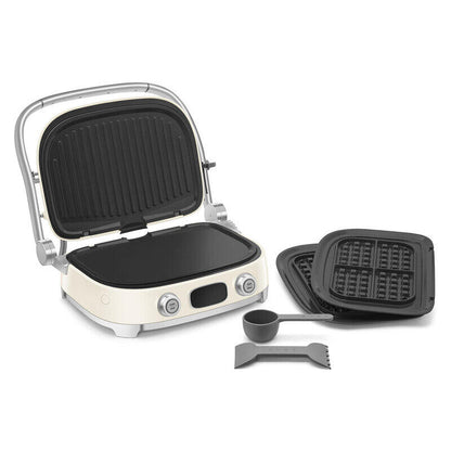 An open cream-colored electric waffle grill with black plates, shown alongside two closed waffle plates and two gray silicone accessories on a plain white background.