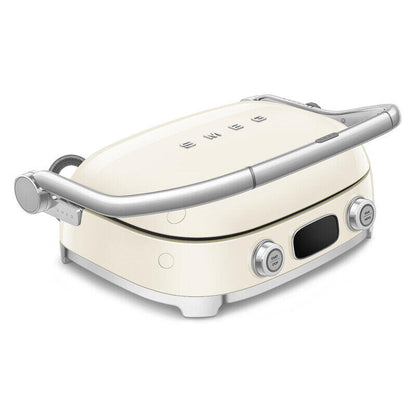 A cream-colored SMEG sandwich grill with silver metal handles and control knobs, shown from a high angle on a white background.
